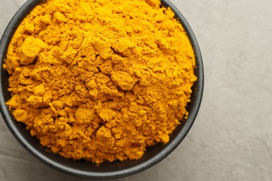 Photo of Turmeric powder in bowl on grey table, closeup. Top view