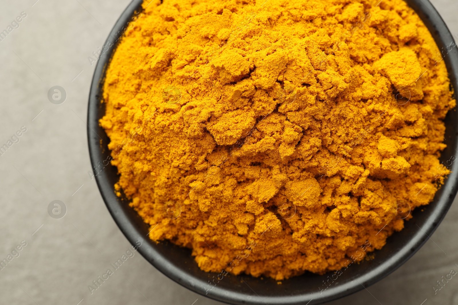 Photo of Turmeric powder in bowl on grey table, closeup. Top view