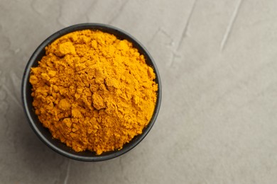 Photo of Turmeric powder in bowl on grey table, top view. Space for text