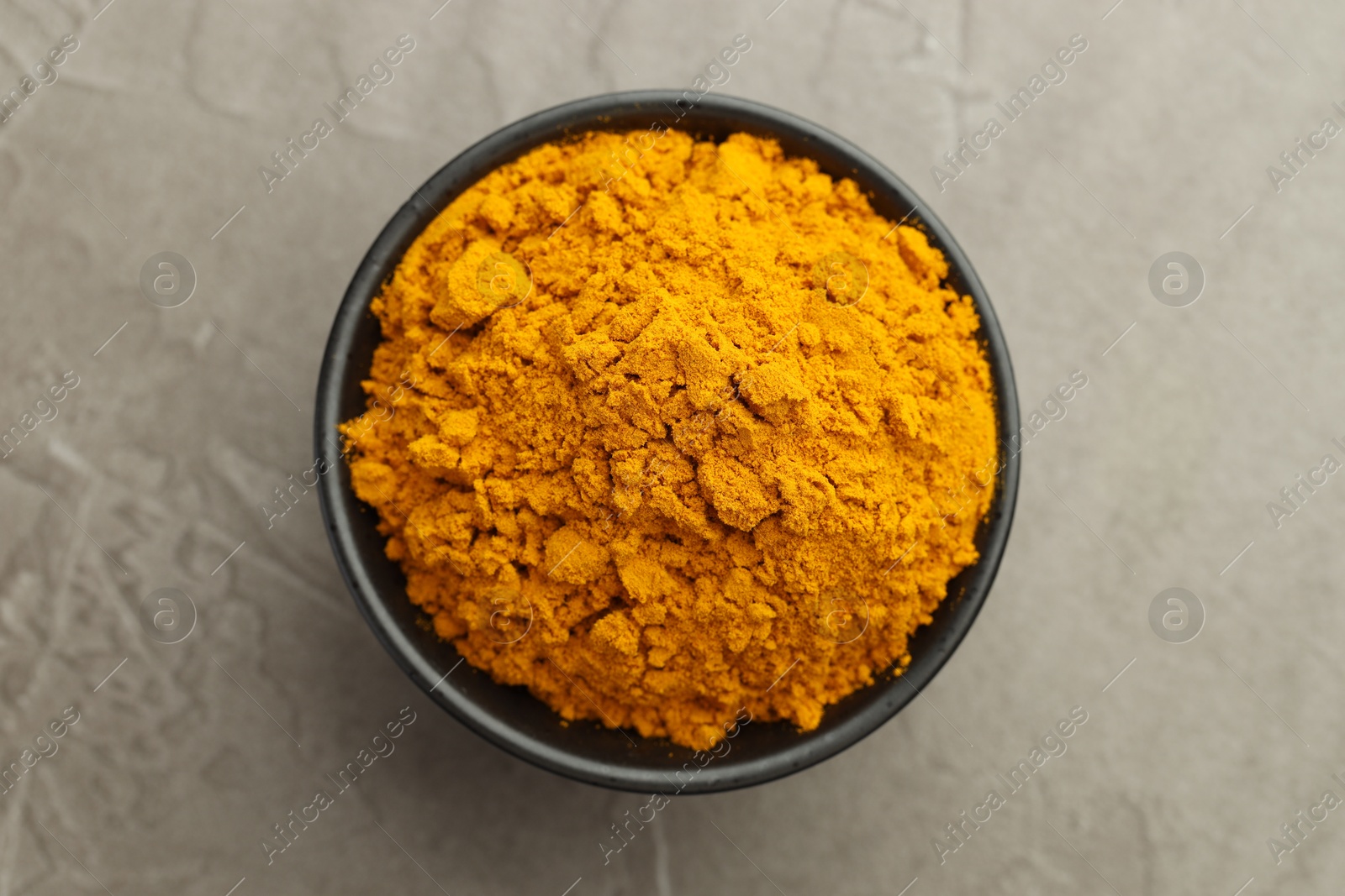 Photo of Turmeric powder in bowl on grey table, top view