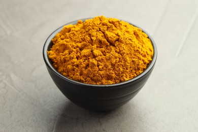 Photo of Turmeric powder in bowl on grey table, closeup