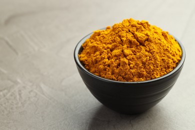 Photo of Turmeric powder in bowl on grey table, closeup. Space for text