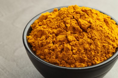 Photo of Turmeric powder in bowl on grey table, closeup