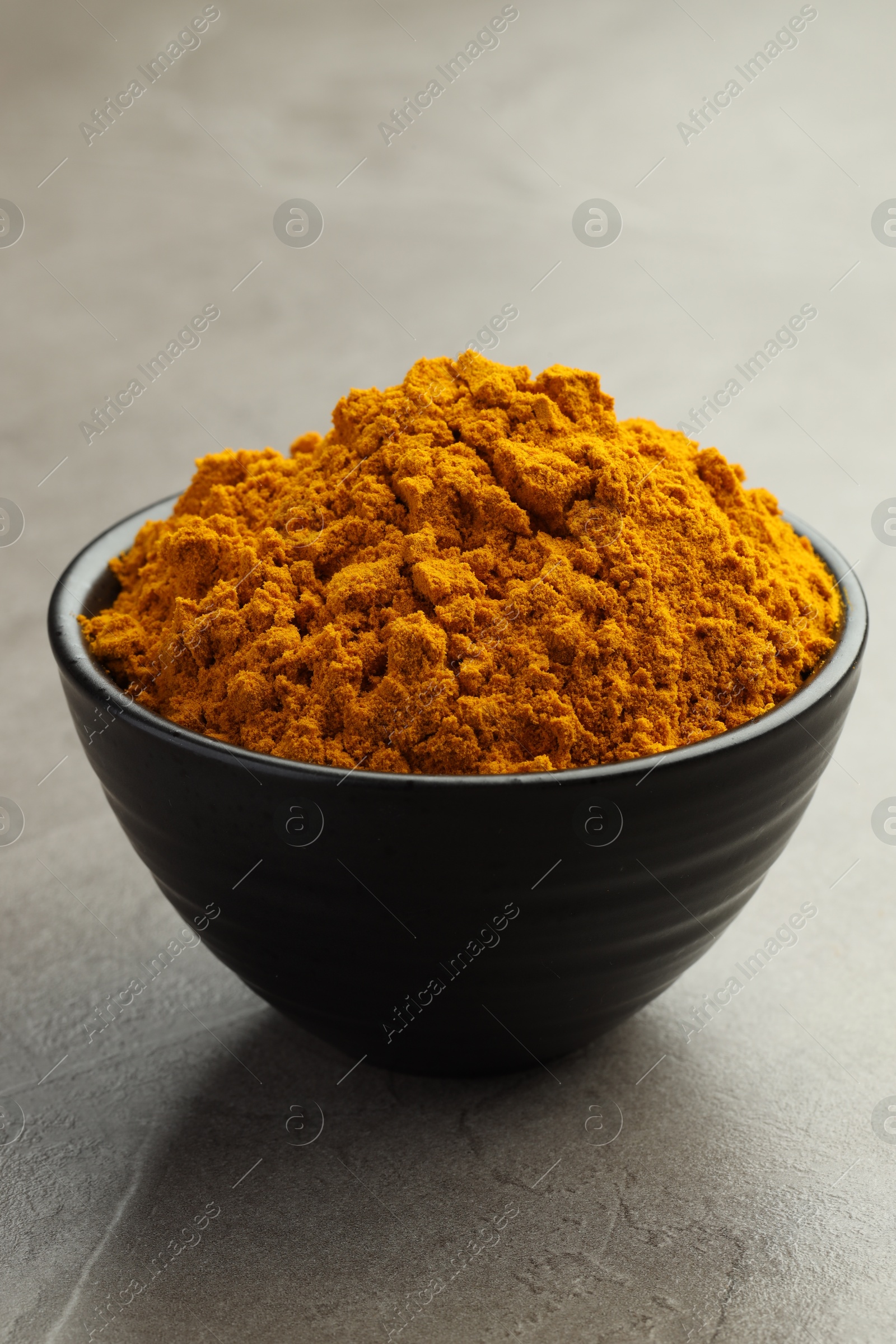 Photo of Turmeric powder in bowl on grey table, closeup