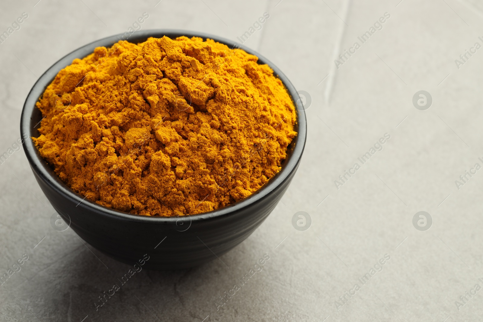 Photo of Turmeric powder in bowl on grey table, closeup. Space for text