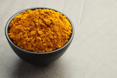 Photo of Turmeric powder in bowl on grey table, closeup. Space for text