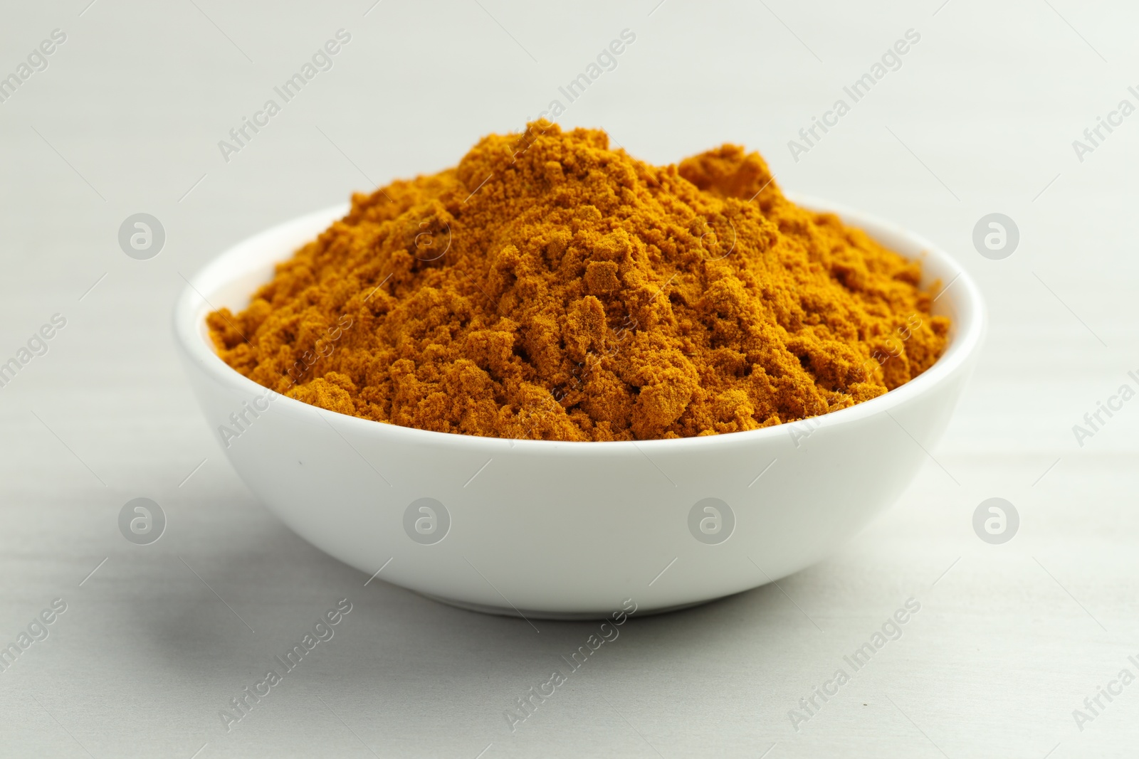 Photo of Turmeric powder in bowl on white table, closeup