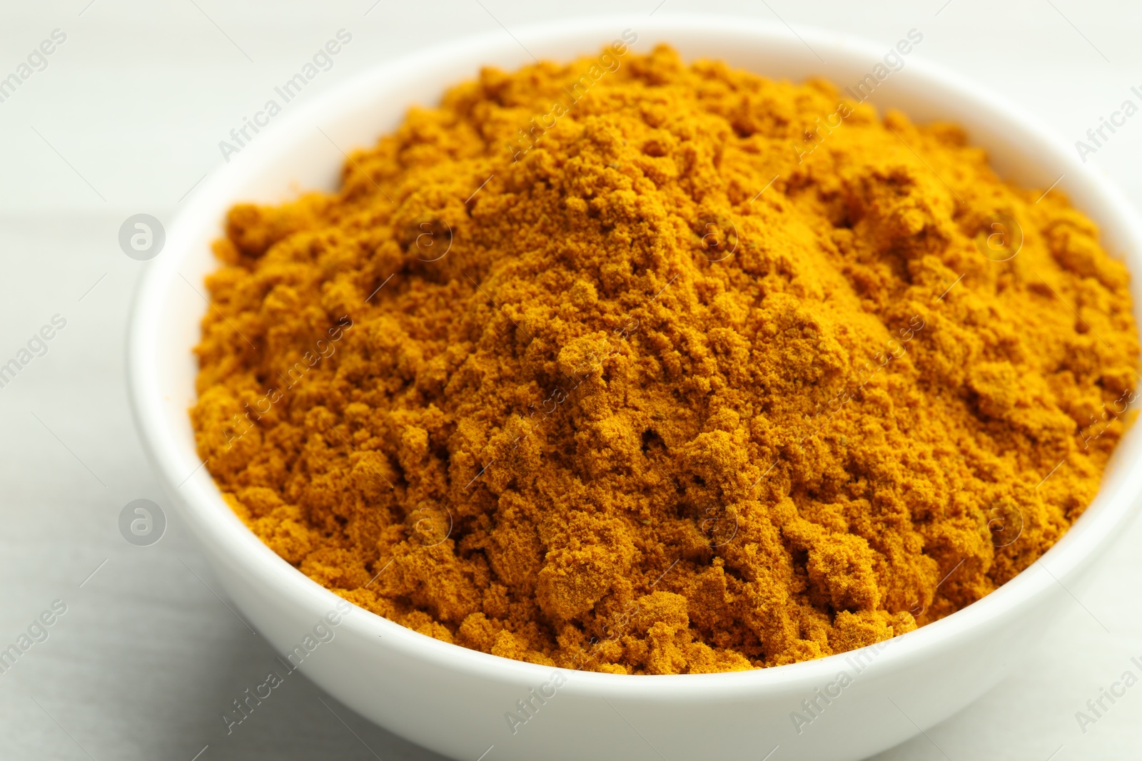 Photo of Turmeric powder in bowl on white table, closeup