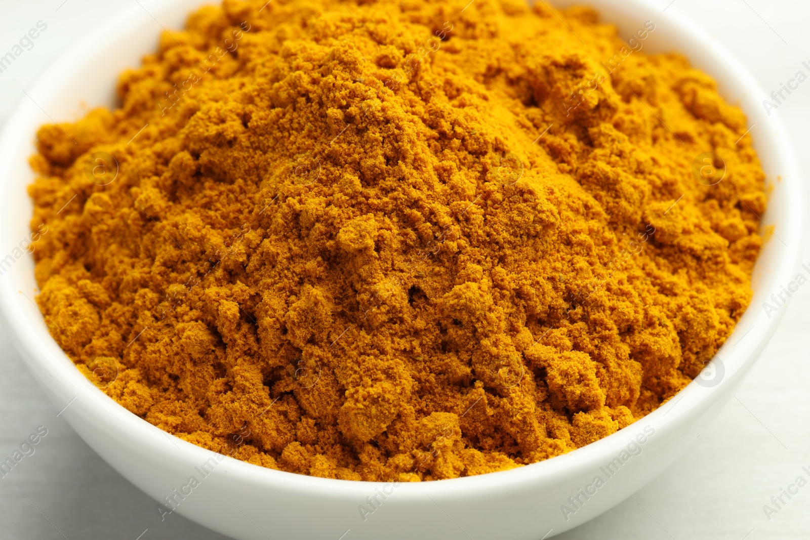 Photo of Turmeric powder in bowl on white table, closeup