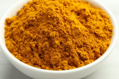 Photo of Turmeric powder in bowl on white table, closeup