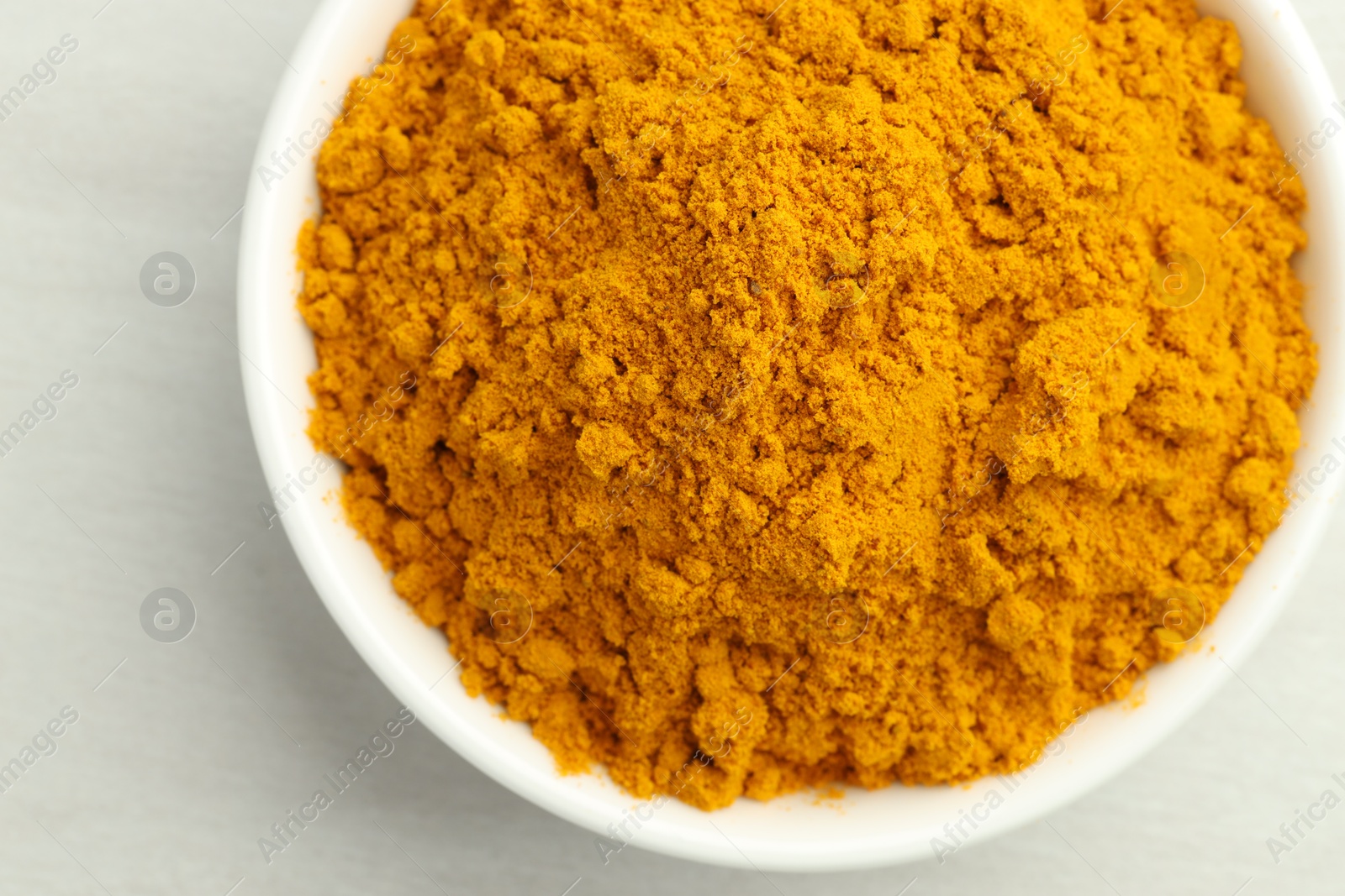 Photo of Turmeric powder in bowl on white table, closeup. Top view