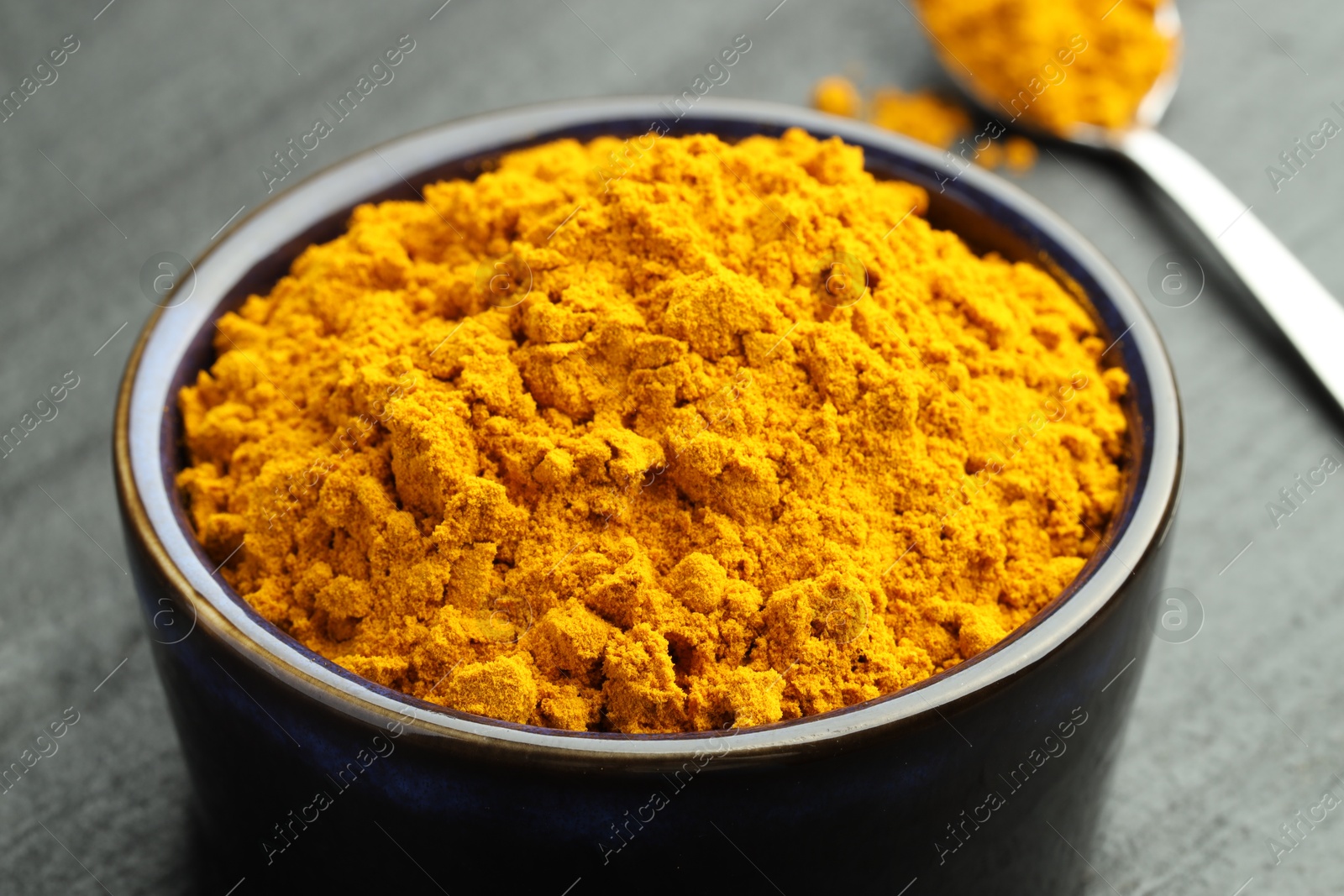 Photo of Turmeric powder in bowl on grey table, closeup