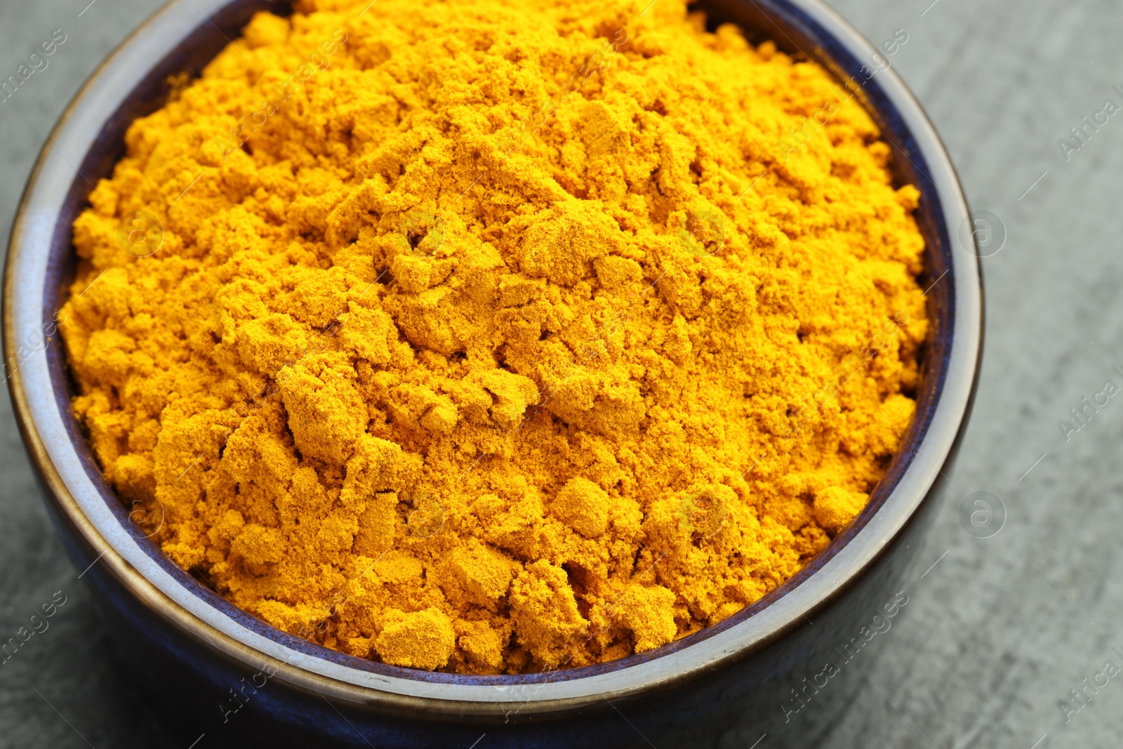 Photo of Turmeric powder in bowl on grey table, closeup