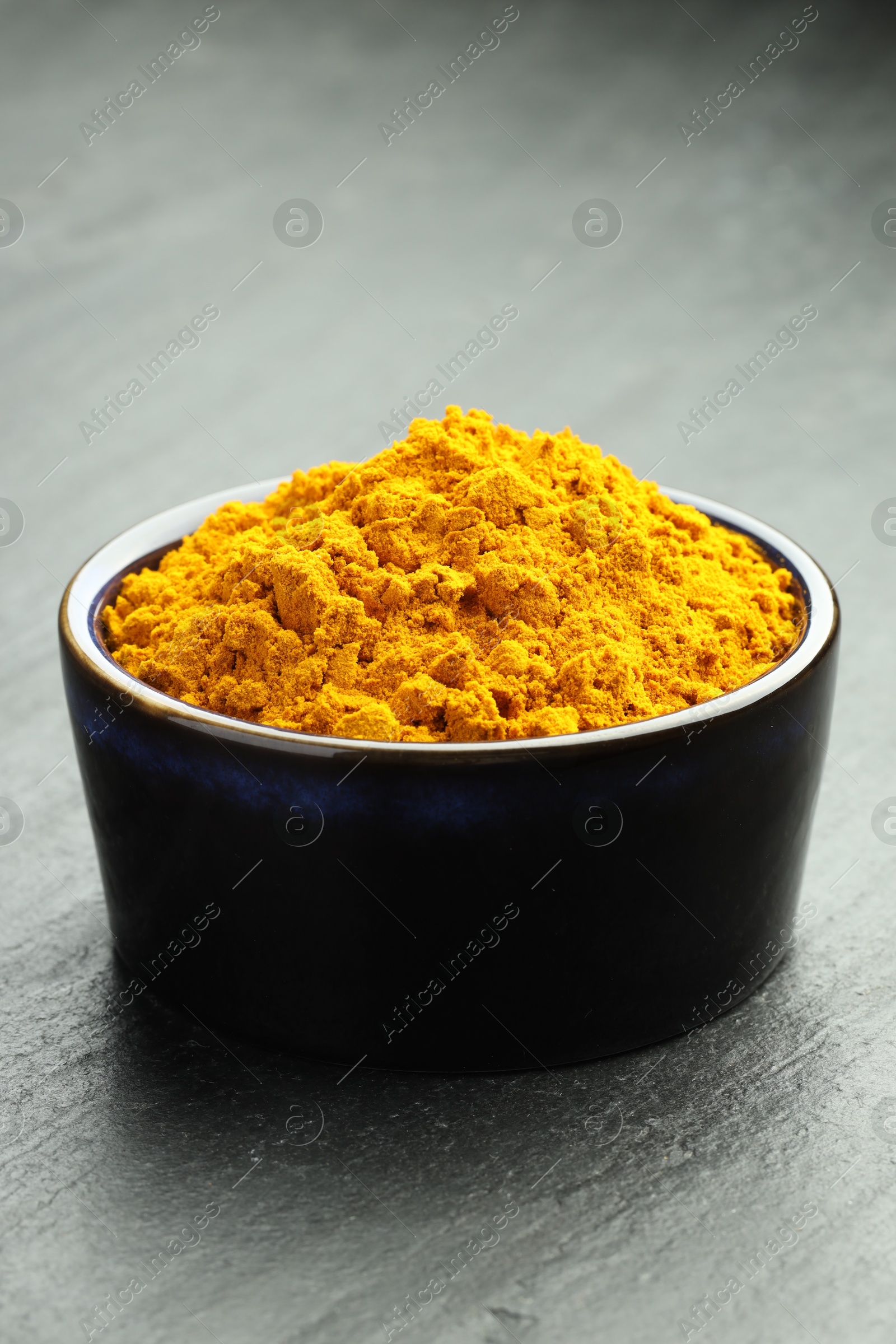 Photo of Turmeric powder in bowl on grey table, closeup