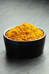 Photo of Turmeric powder in bowl on grey table, closeup