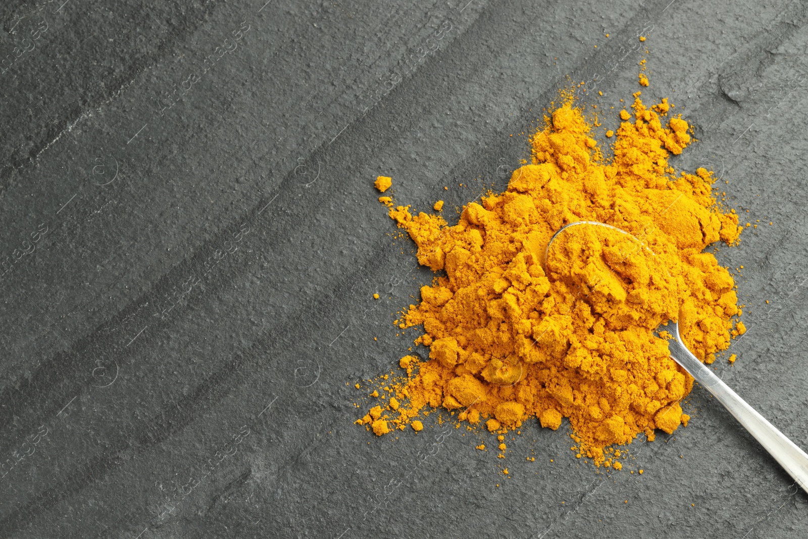 Photo of Turmeric powder and spoon on grey table, top view. Space for text