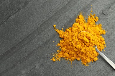 Photo of Turmeric powder and spoon on grey table, top view. Space for text