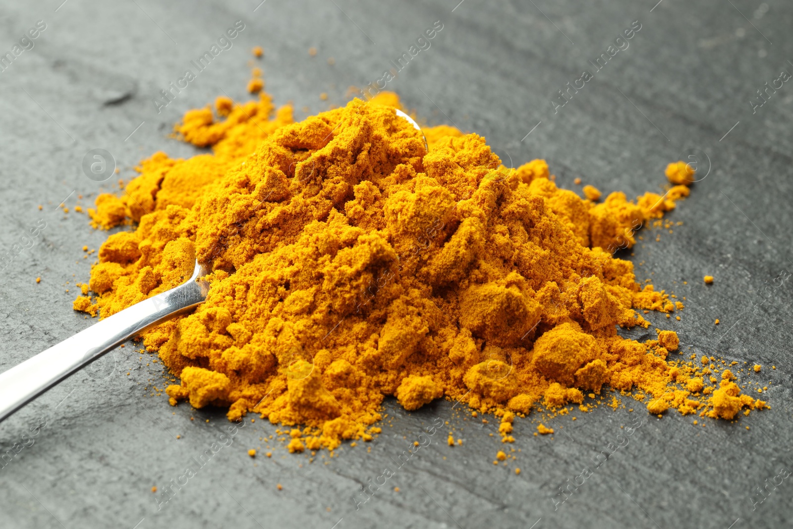 Photo of Turmeric powder and spoon on grey table, closeup