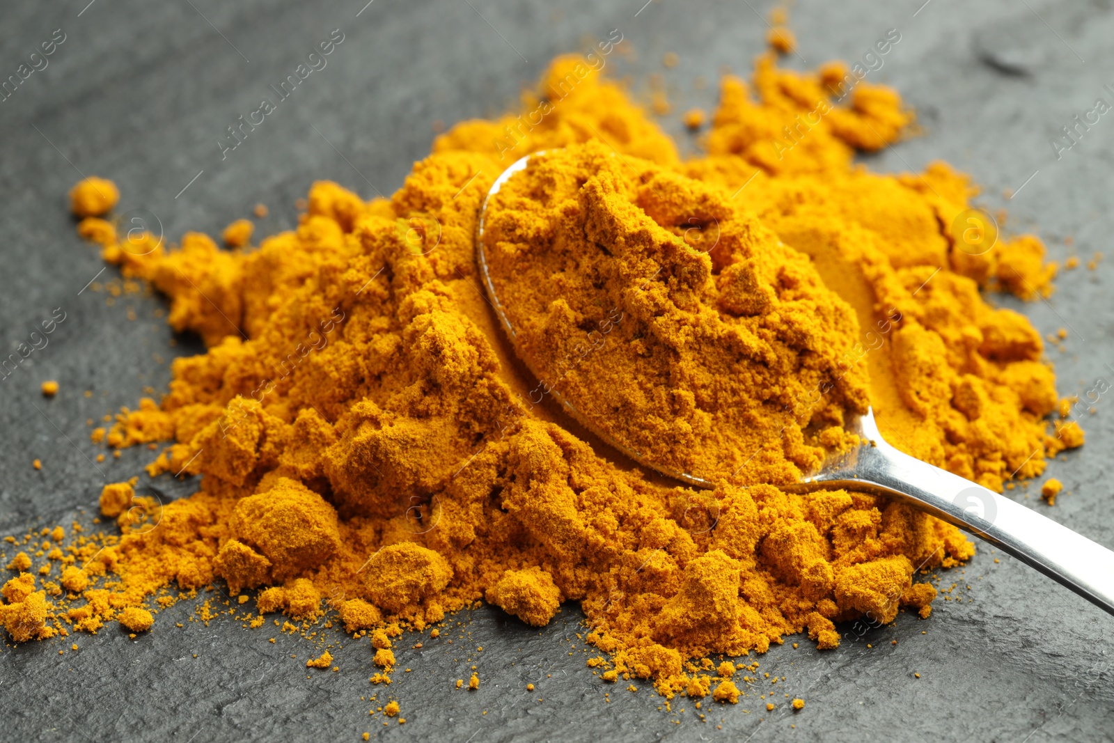 Photo of Turmeric powder and spoon on grey table, closeup