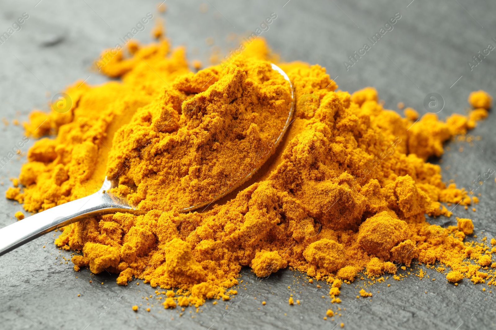 Photo of Turmeric powder and spoon on grey table, closeup