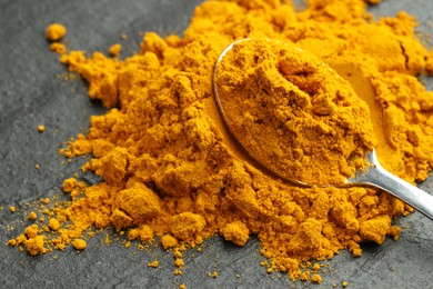 Photo of Turmeric powder and spoon on grey table, closeup