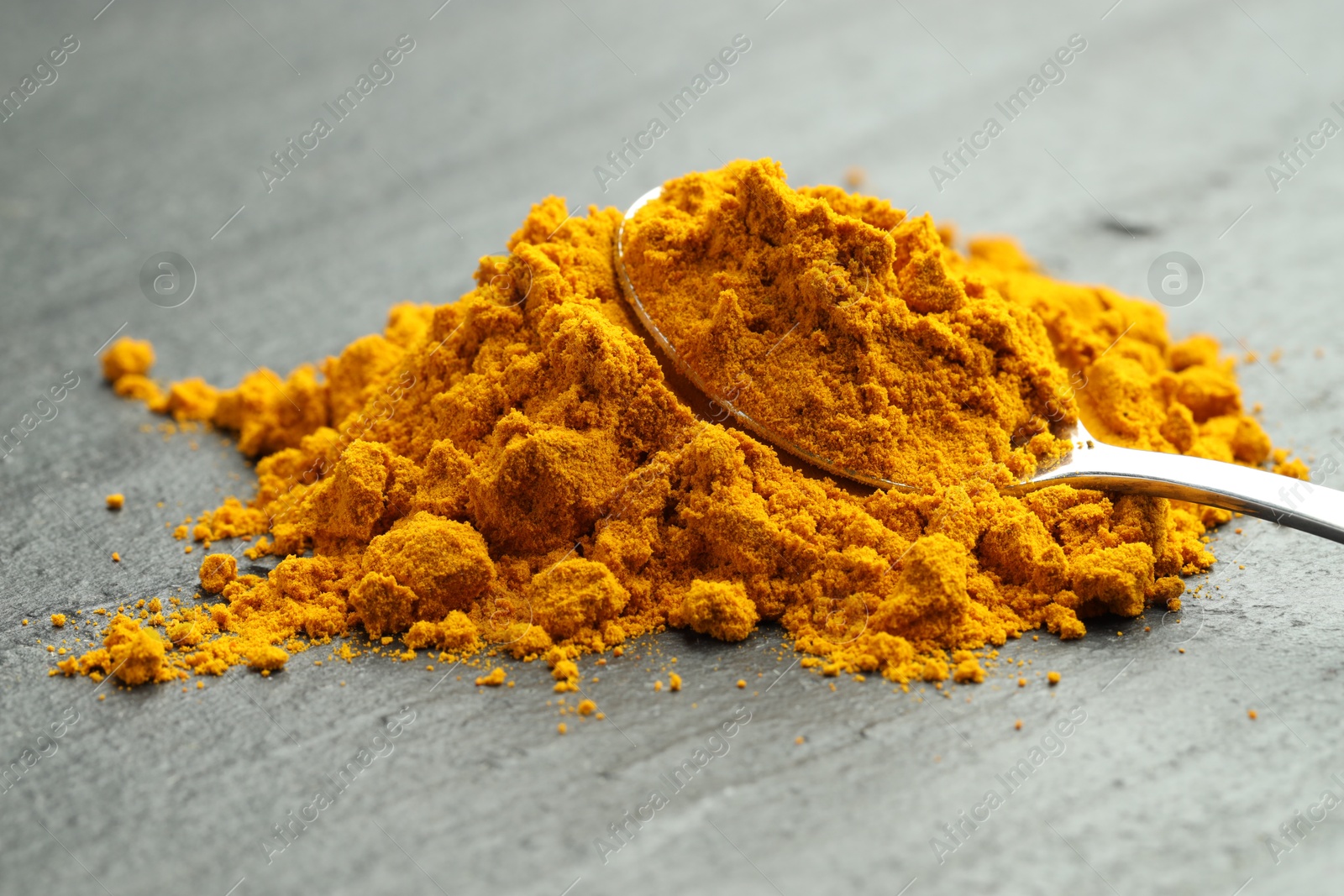 Photo of Turmeric powder and spoon on grey table, closeup