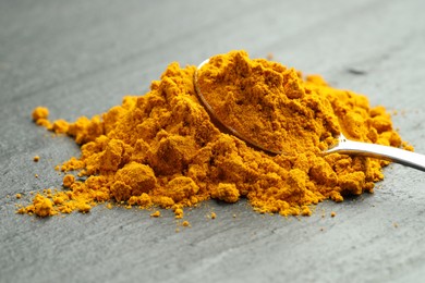 Photo of Turmeric powder and spoon on grey table, closeup