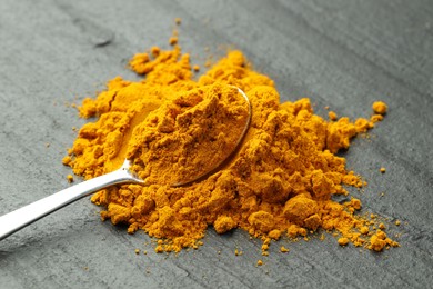 Photo of Turmeric powder and spoon on grey table, closeup