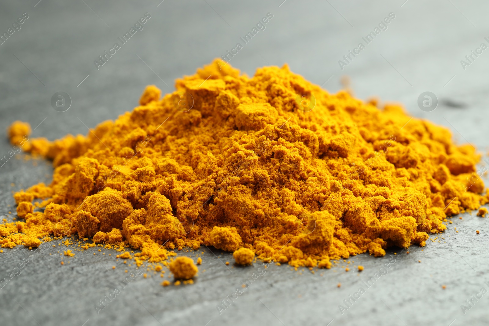 Photo of Heap of turmeric powder on grey table, closeup