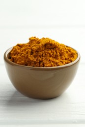 Photo of Turmeric powder in bowl on white wooden table, closeup