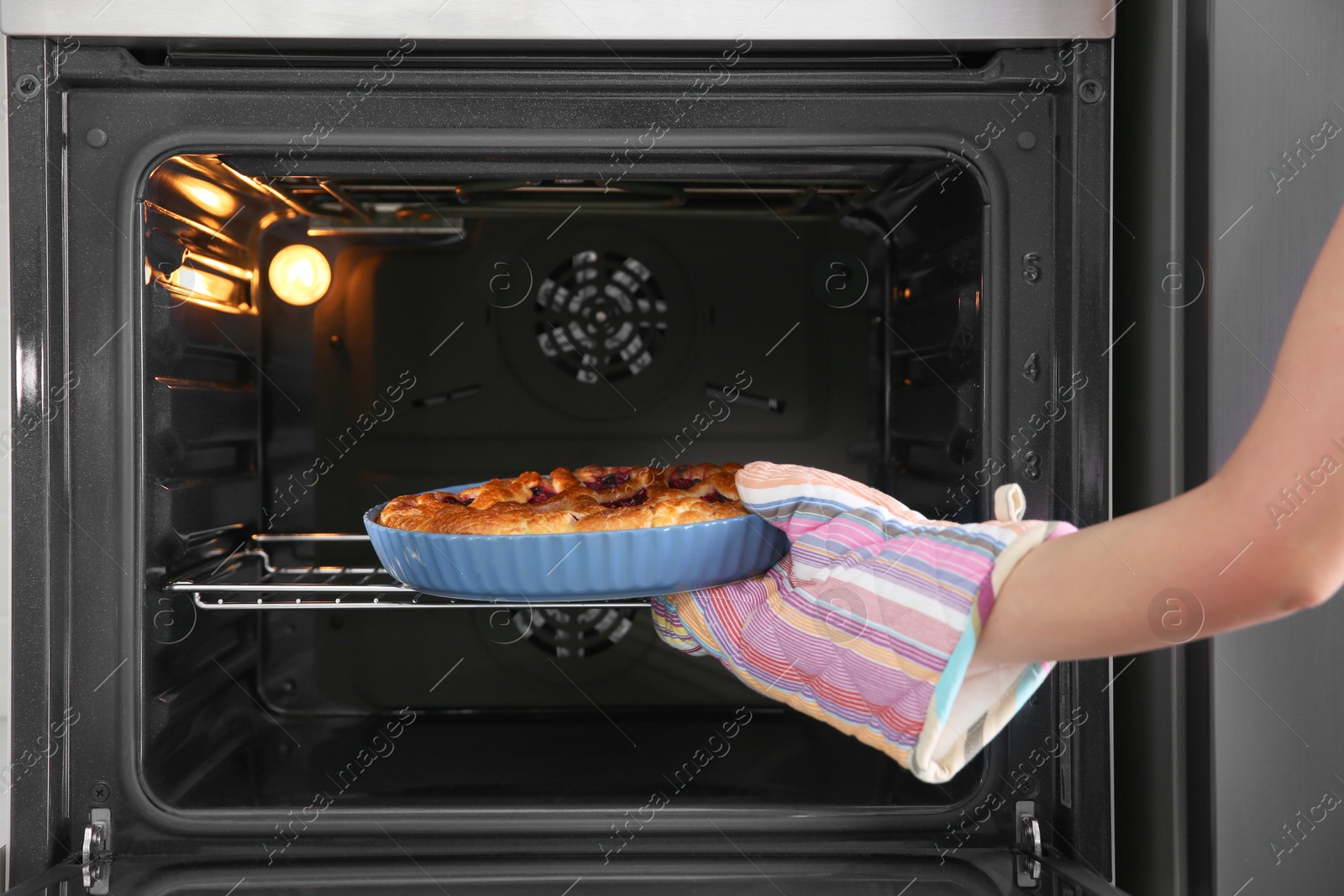 Photo of Woman taking delicious currant pie out of oven, closeup