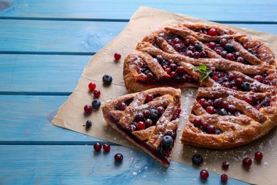 Photo of Delicious cut currant pie and fresh berries on blue wooden table, space for text