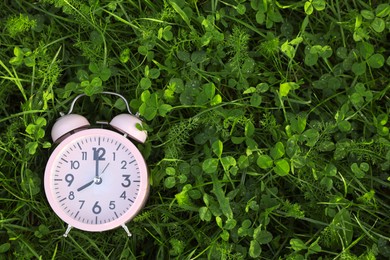 Photo of Pink small alarm clock on green grass outdoors, top view. Space for text