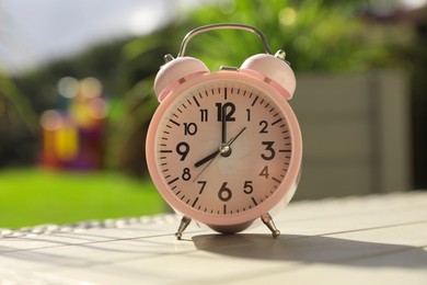 Photo of Pink alarm clock on table outdoors at sunny morning