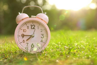 Photo of Pink alarm clock on green grass outdoors. Space for text