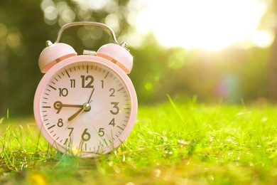 Photo of Pink alarm clock on green grass outdoors. Space for text