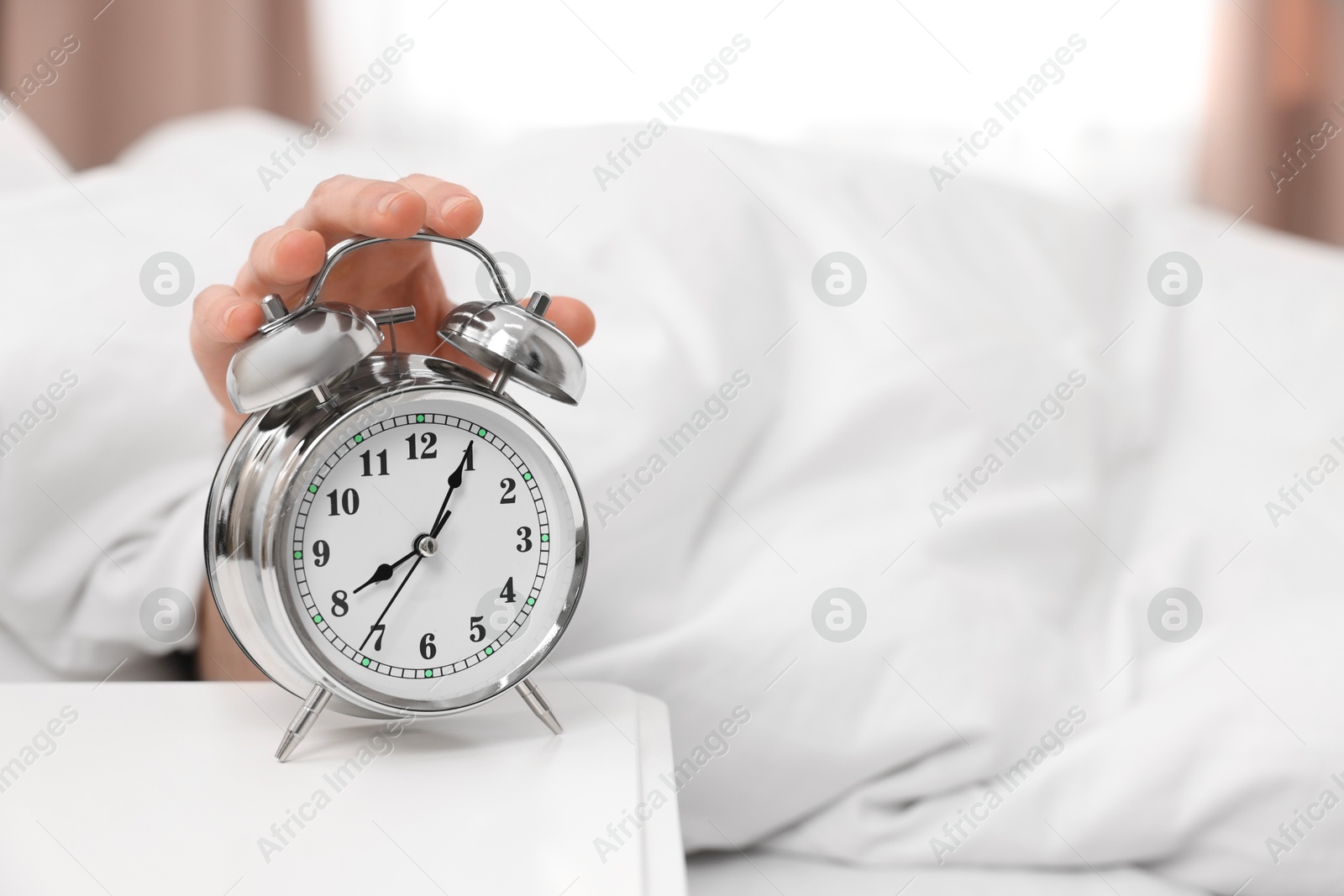 Photo of Man turning off alarm clock in bedroom, focus on hand. Space for text