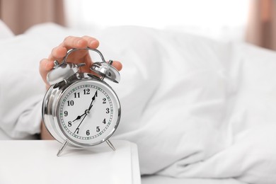 Photo of Man turning off alarm clock in bedroom, focus on hand. Space for text