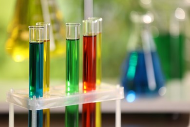 Laboratory test tubes with colorful liquids against blurred background, closeup. Space for text