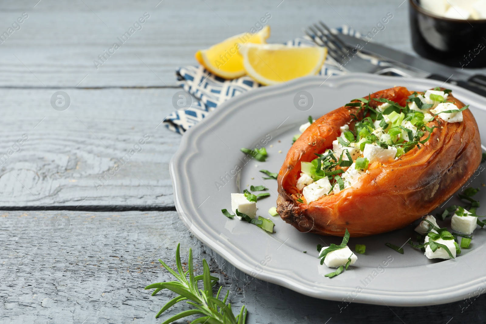 Photo of Tasty cooked sweet potato with feta cheese and green onion on grey wooden table, closeup. Space for text