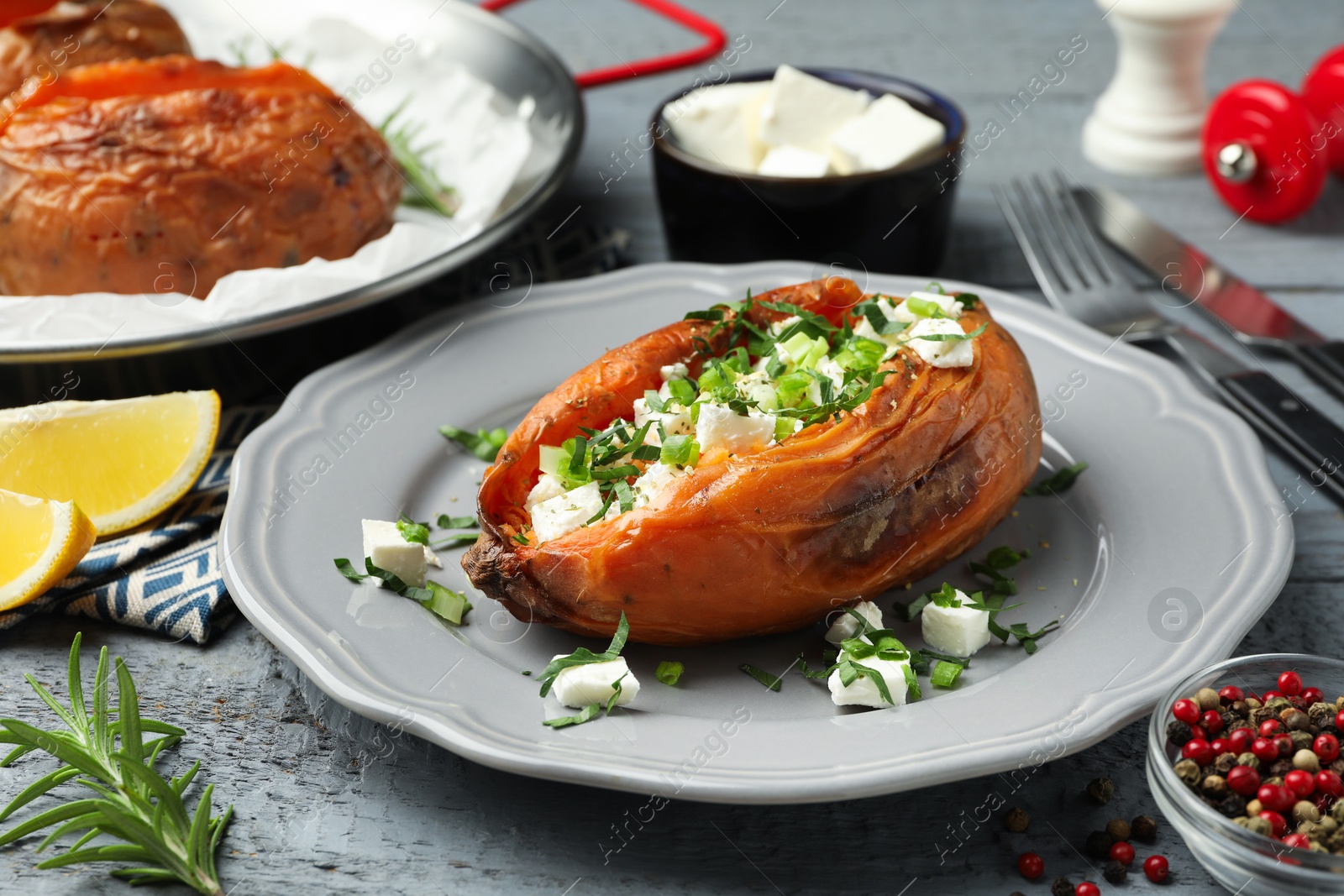 Photo of Tasty cooked sweet potatoes served with feta cheese on grey wooden table, closeup