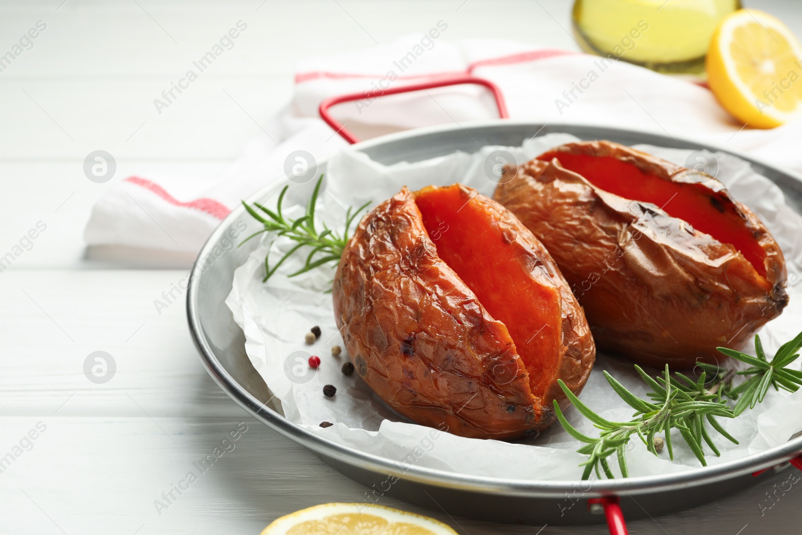 Photo of Tasty cooked sweet potatoes served with rosemary on white wooden table, closeup