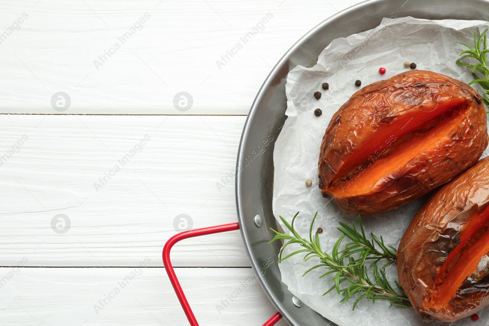 Photo of Tasty cooked sweet potatoes with rosemary on white wooden table, top view. Space for text