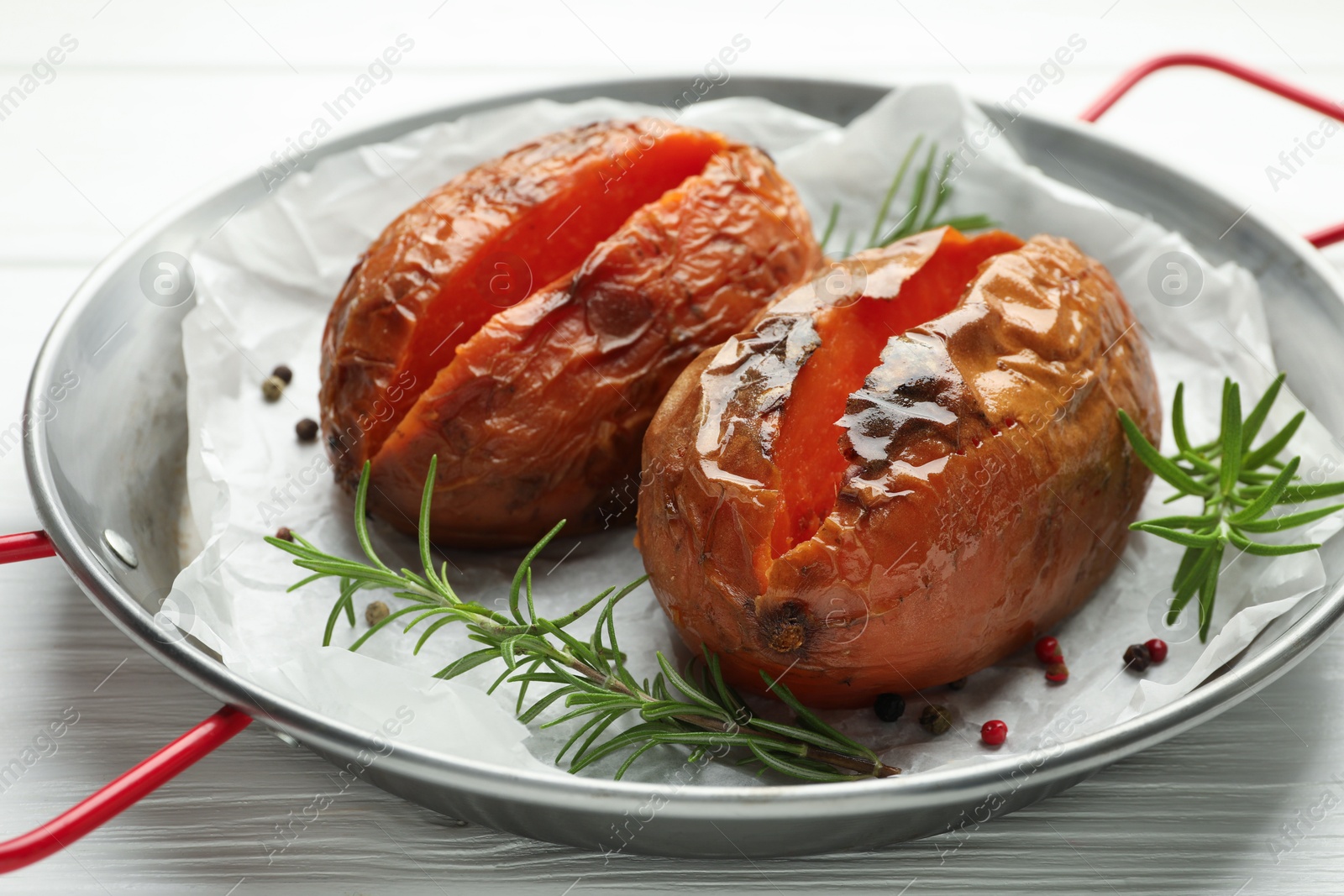 Photo of Tasty cooked sweet potatoes with rosemary on white wooden table, closeup