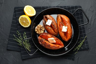 Photo of Tasty cooked sweet potatoes with feta cheese, garlic, thyme and lemon on black table, top view