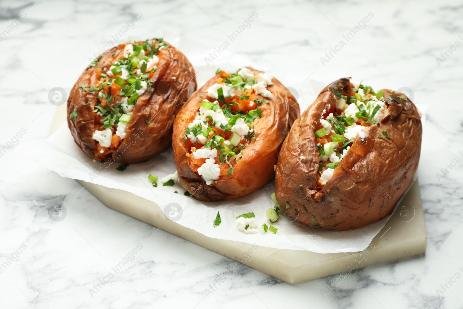 Photo of Tasty cooked sweet potatoes with feta cheese, green onion and parsley on white marble table, closeup