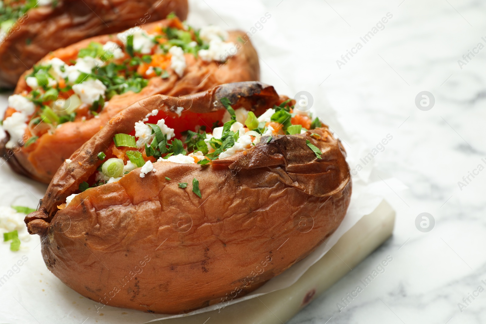 Photo of Tasty cooked sweet potatoes with feta cheese, green onion and parsley on white marble table, closeup