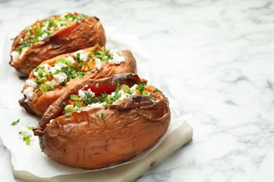 Photo of Tasty cooked sweet potatoes with feta cheese, green onion and parsley on white marble table, closeup. Space for text