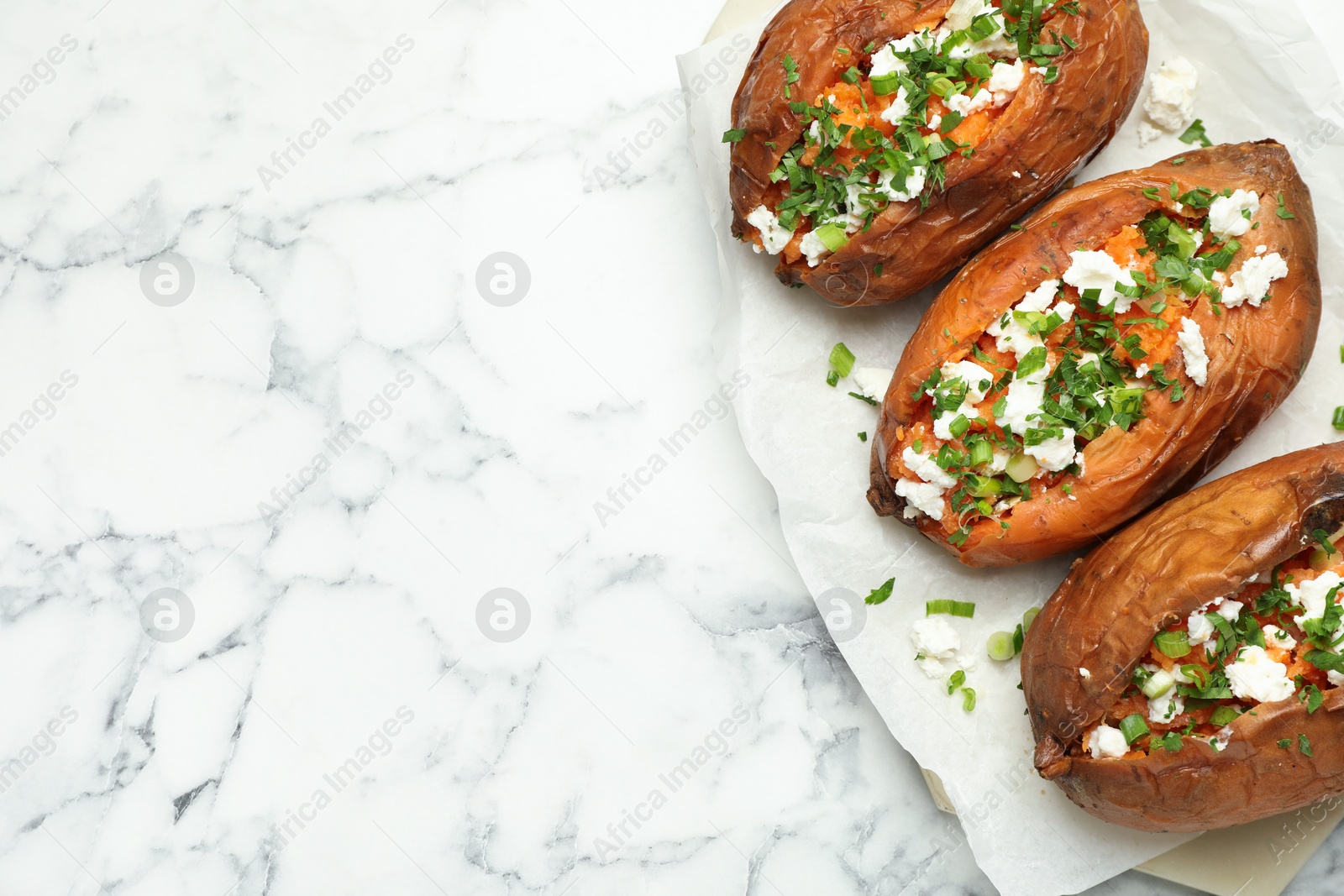 Photo of Tasty cooked sweet potatoes with feta cheese, green onion and parsley on white marble table, top view. Space for text