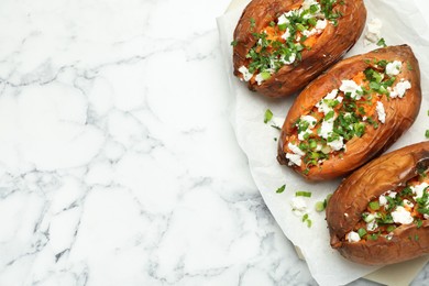 Photo of Tasty cooked sweet potatoes with feta cheese, green onion and parsley on white marble table, top view. Space for text